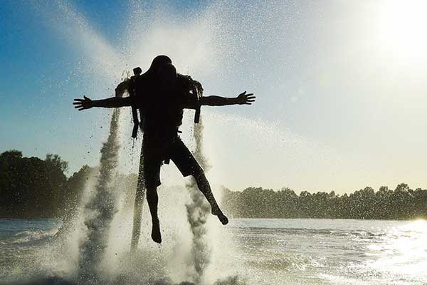 The silhouette of a man up in the air using a water jetpack on a river