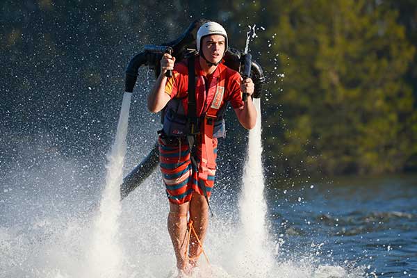 A young man hovering above the water using a water powered jet pack