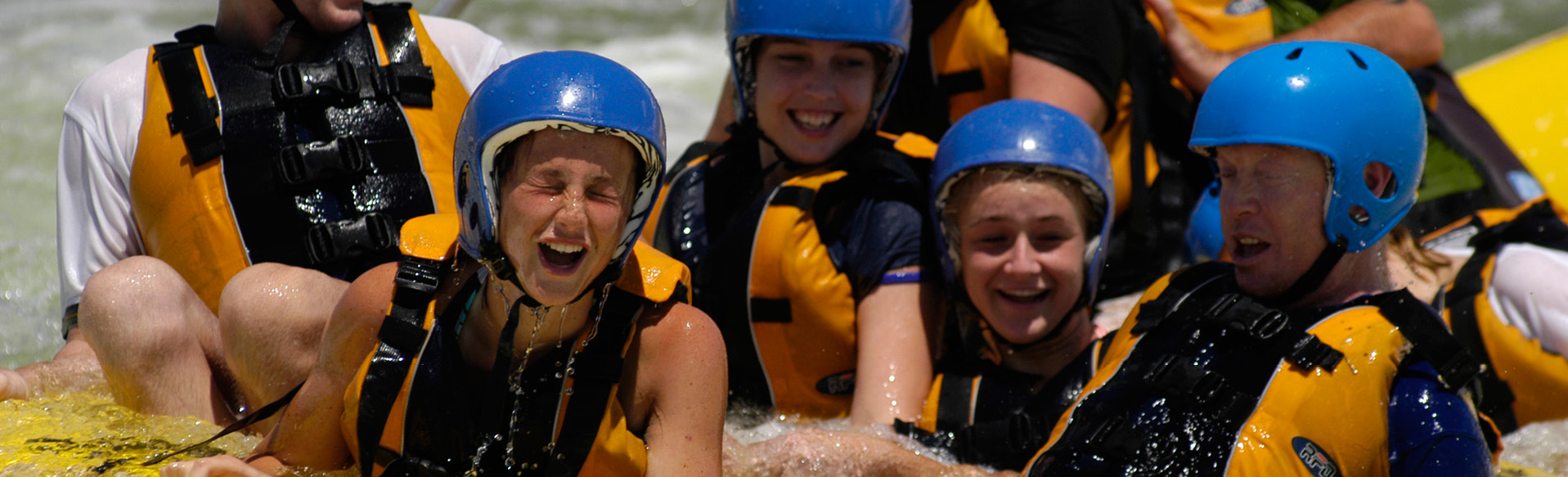 A group of young girls in a raft sailing down a wild white water river with safety gear on