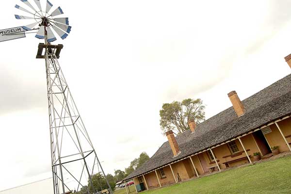 A large windmill standing beside a historic heritage building with various brick chimneys
