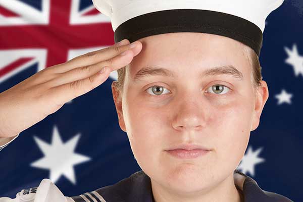 Young boy dressed in marine uniform saluting in front of an Australian flag