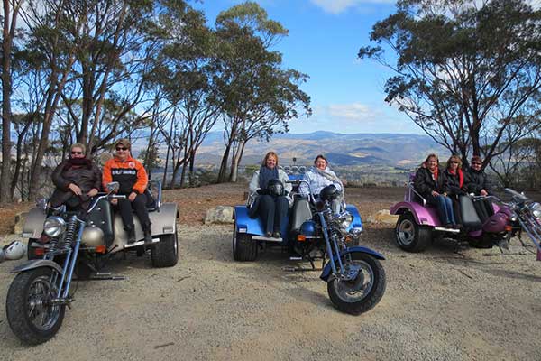 Group of people sitting on motor tricycles in front of a mountain view